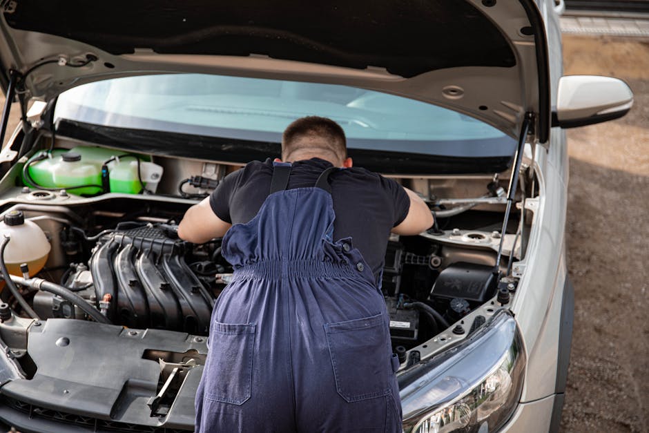 Mechanic in overalls working on a car engine outdoors, offering vehicle repair services.